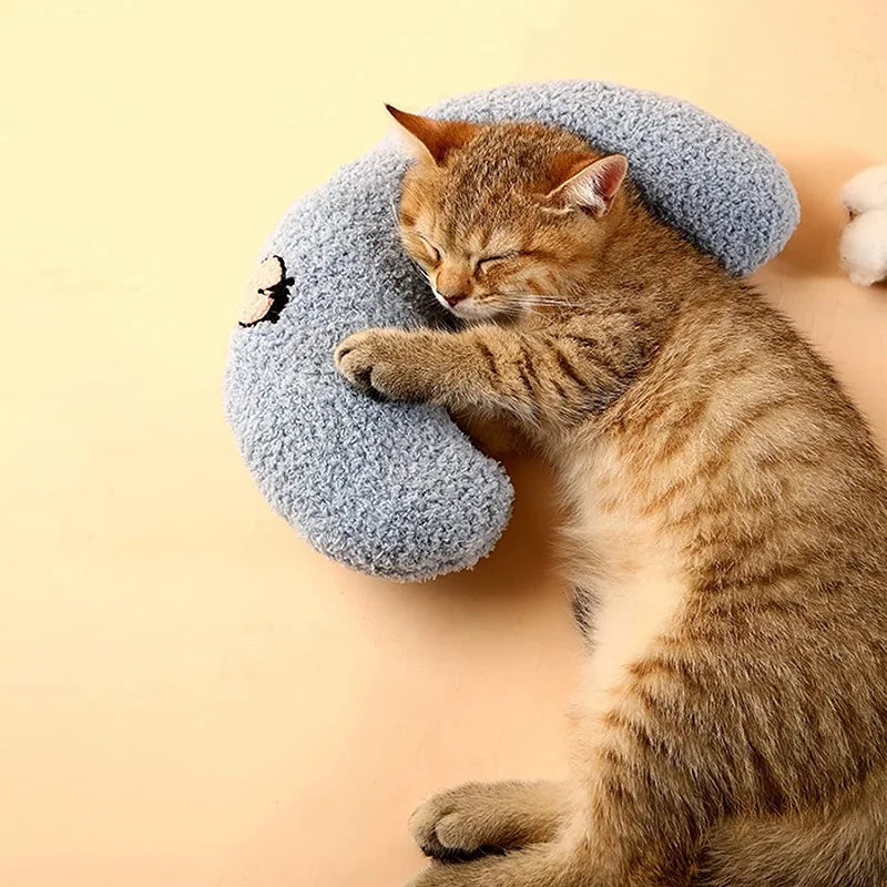 Coussin pour chat couleur bleu un chat dort paisiblement sur un oreiller ergonomique, offrant confort et sécurité grâce à sa forme demi-lune et sa fausse fourrure douce.