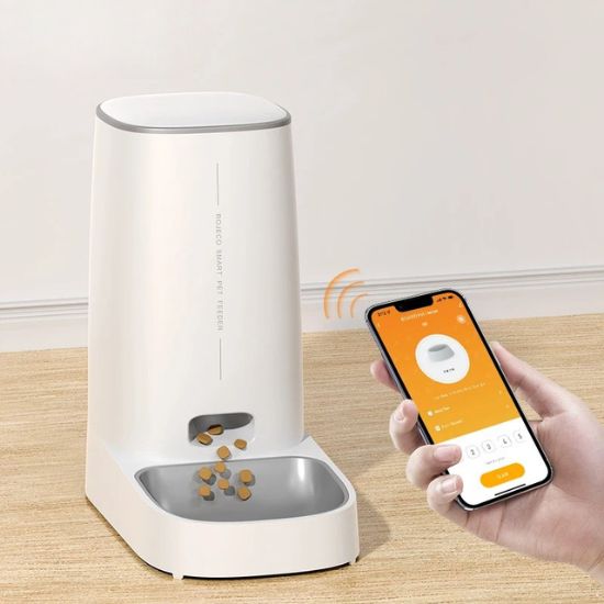 Distributeur croquette chat automatique, main tenant un téléphone près du distributeur, illustrant l'application mobile pour programmer les repas.