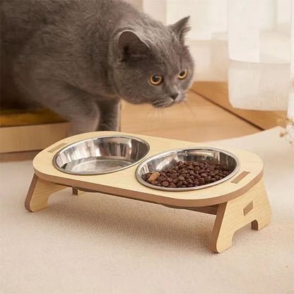 gamelle chat bol inox support bois surélevé avec deux bols un rempli de croquettes chat gris british shorthair s'incline vers le support sur sol intérieur