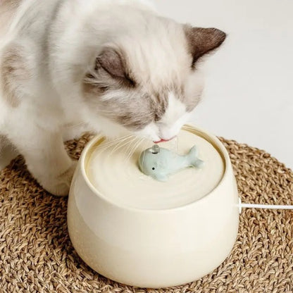 Fontaine à eau chat en céramique ultra-silencieuse beige  avec un chat buvant d'une fontaine avec bec en forme de baleine sur un tapis tissé 